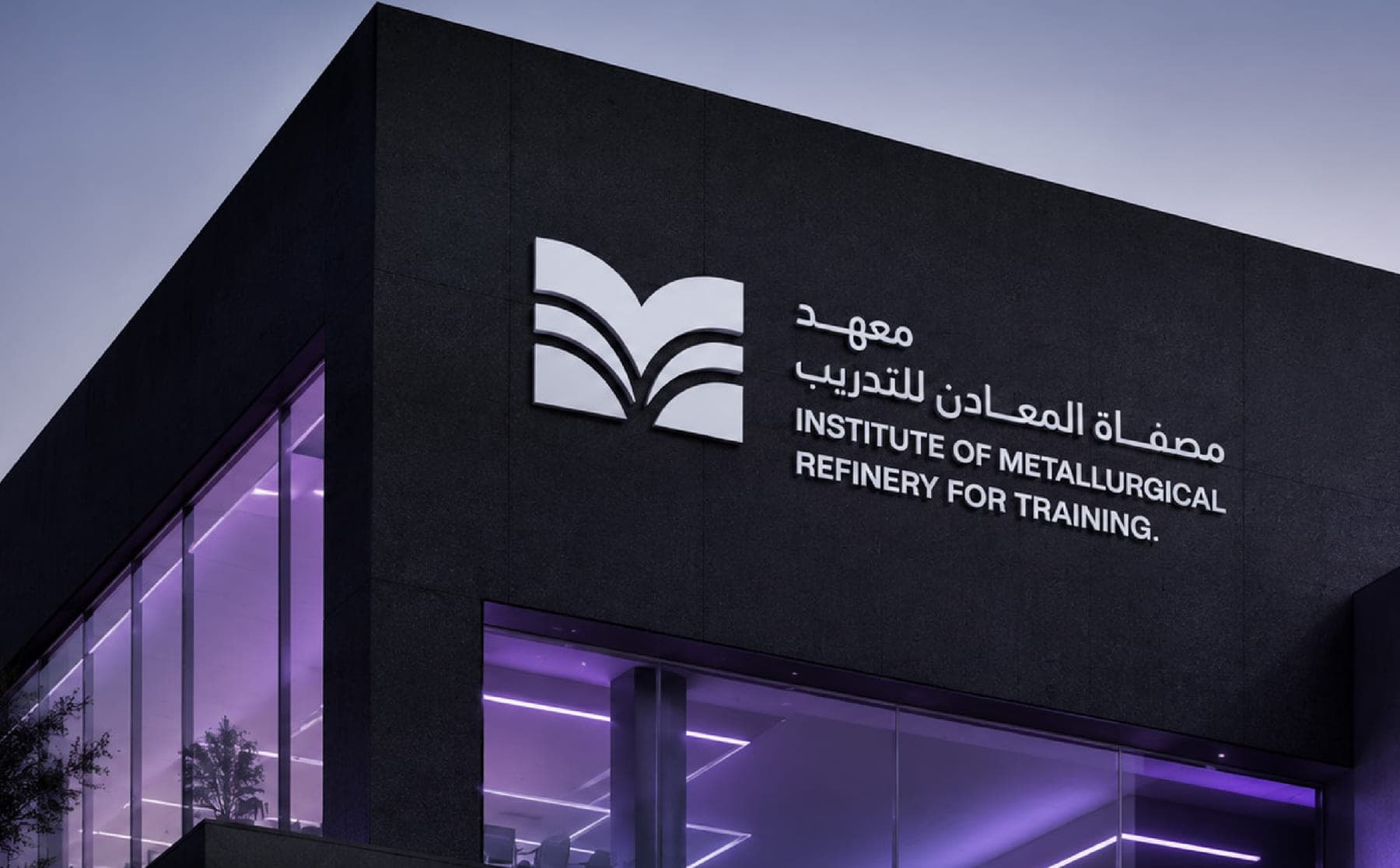 شعار المعهد مثبت على واجهة مبنى داكنة تضيئها إنارة داخلية عند الغروب.